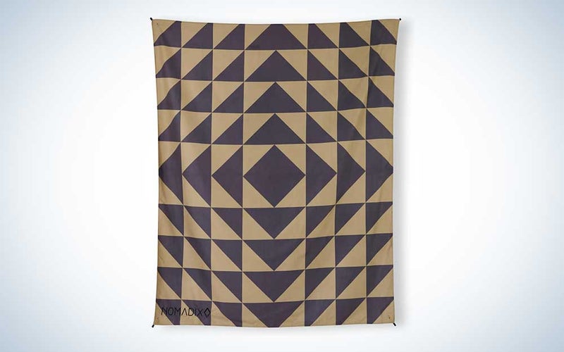 A brown and black Nomadix festival blanket on a plain background.